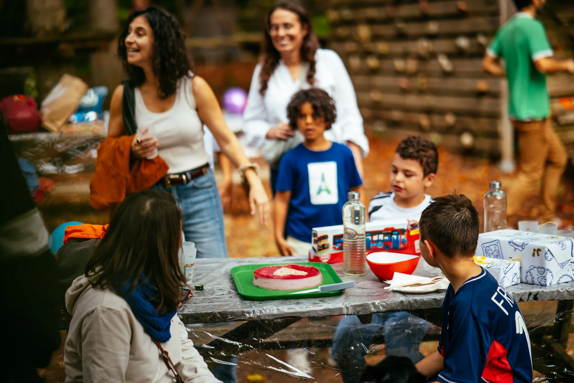 Enfants et parents autour de la table d'anniversaire, avec le gâteau et les cadeaux