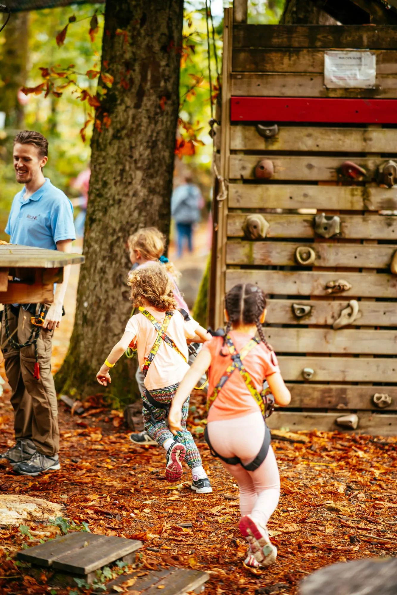Enfants harnachés qui courent dans les feuilles mortes vers le mur d'escalade
